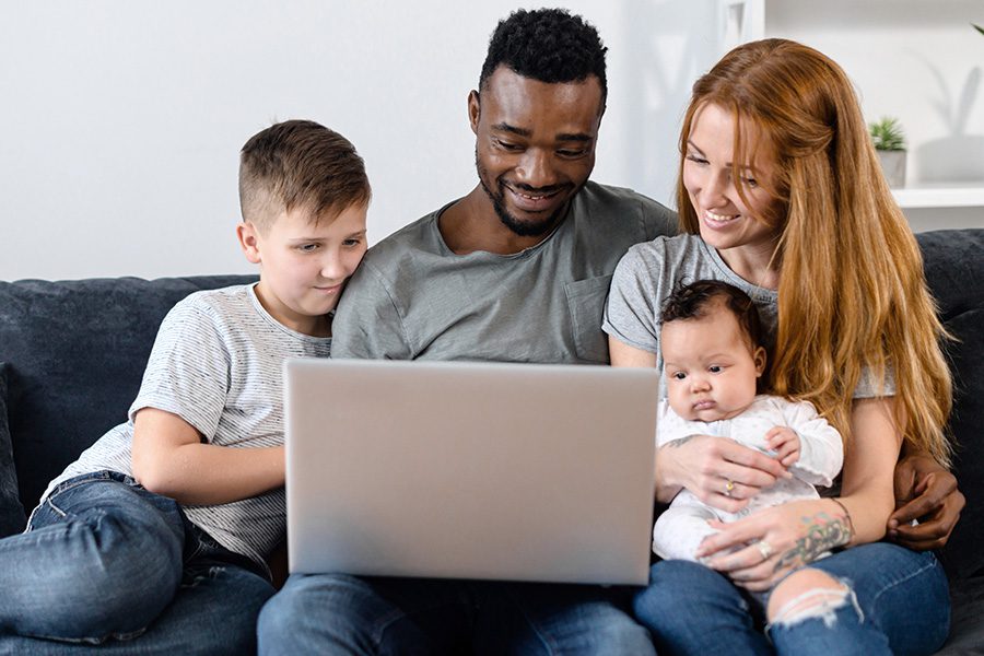 Client Center - A Family and Their Son and Baby Are Sitting Together on a Sofa While Using a Laptop to Video Chat